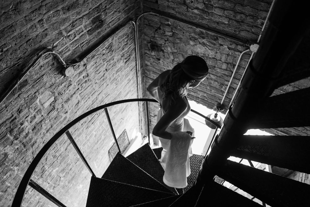 Black and white photo of a person descending a spiral staircase in a brick building.