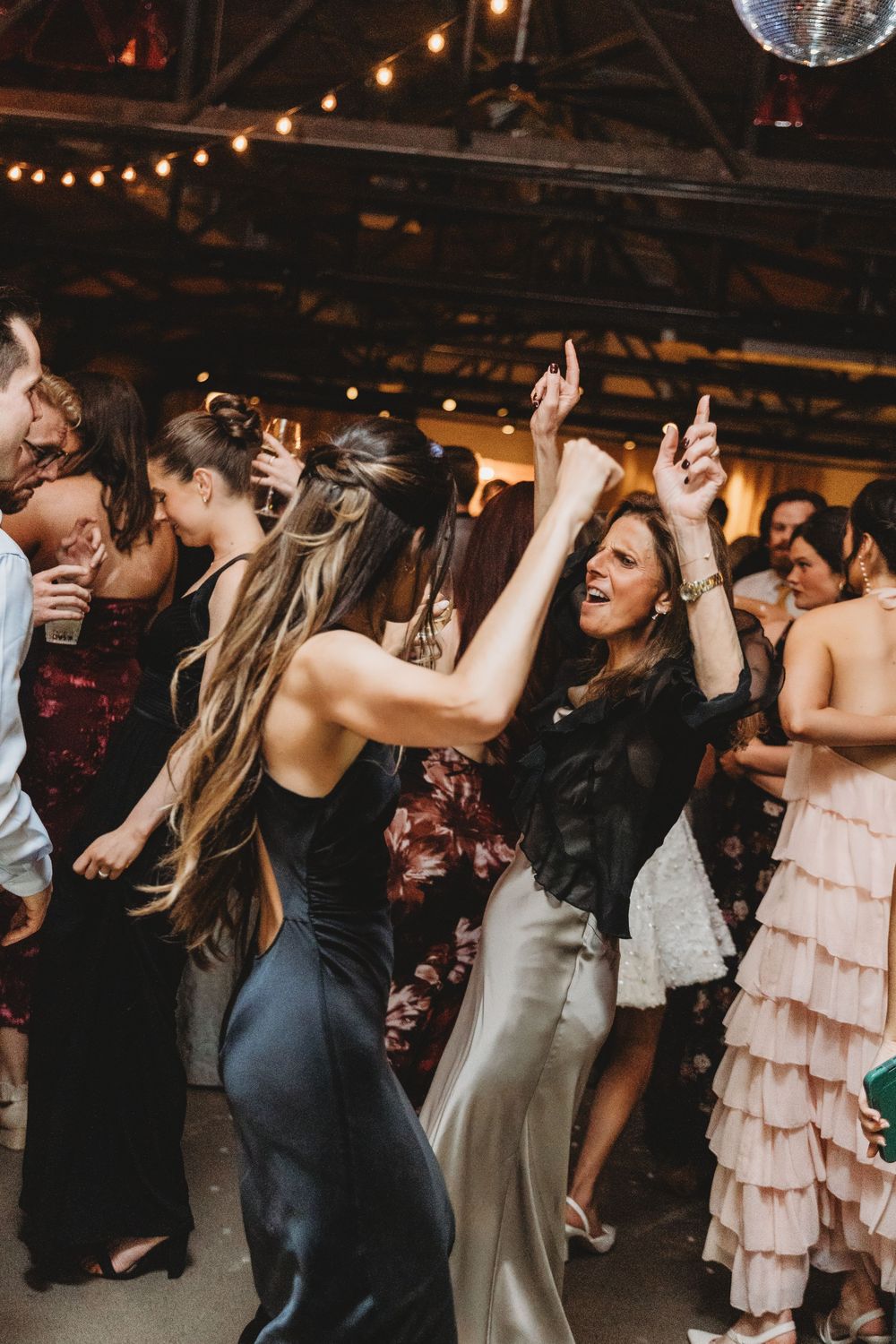 Guests dancing joyfully at a wedding reception under string lights and a disco ball.