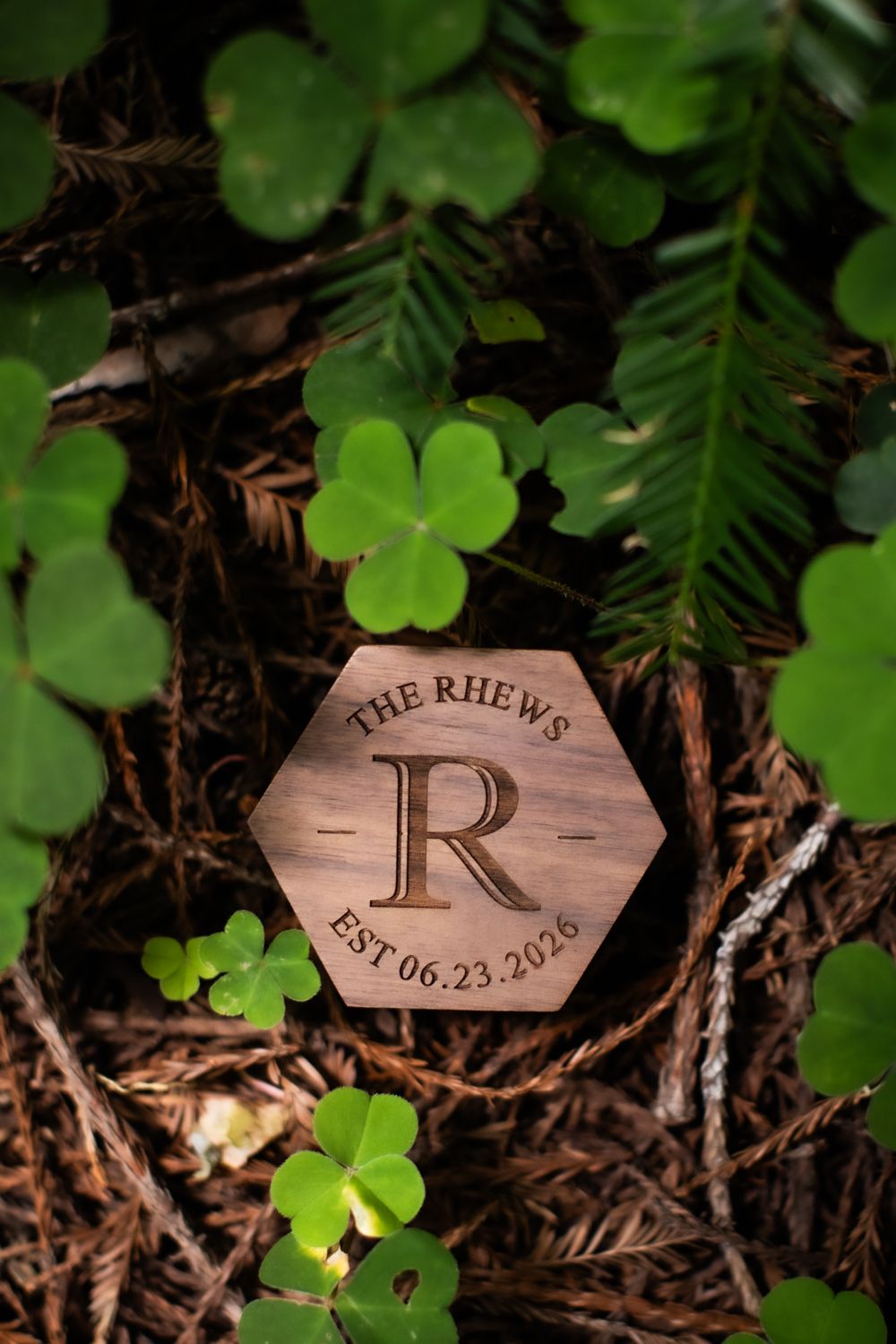 Hexagonal wooden monogram keepsake engraved with The Rhews EST 06.23.2026 surrounded by green clover leaves.