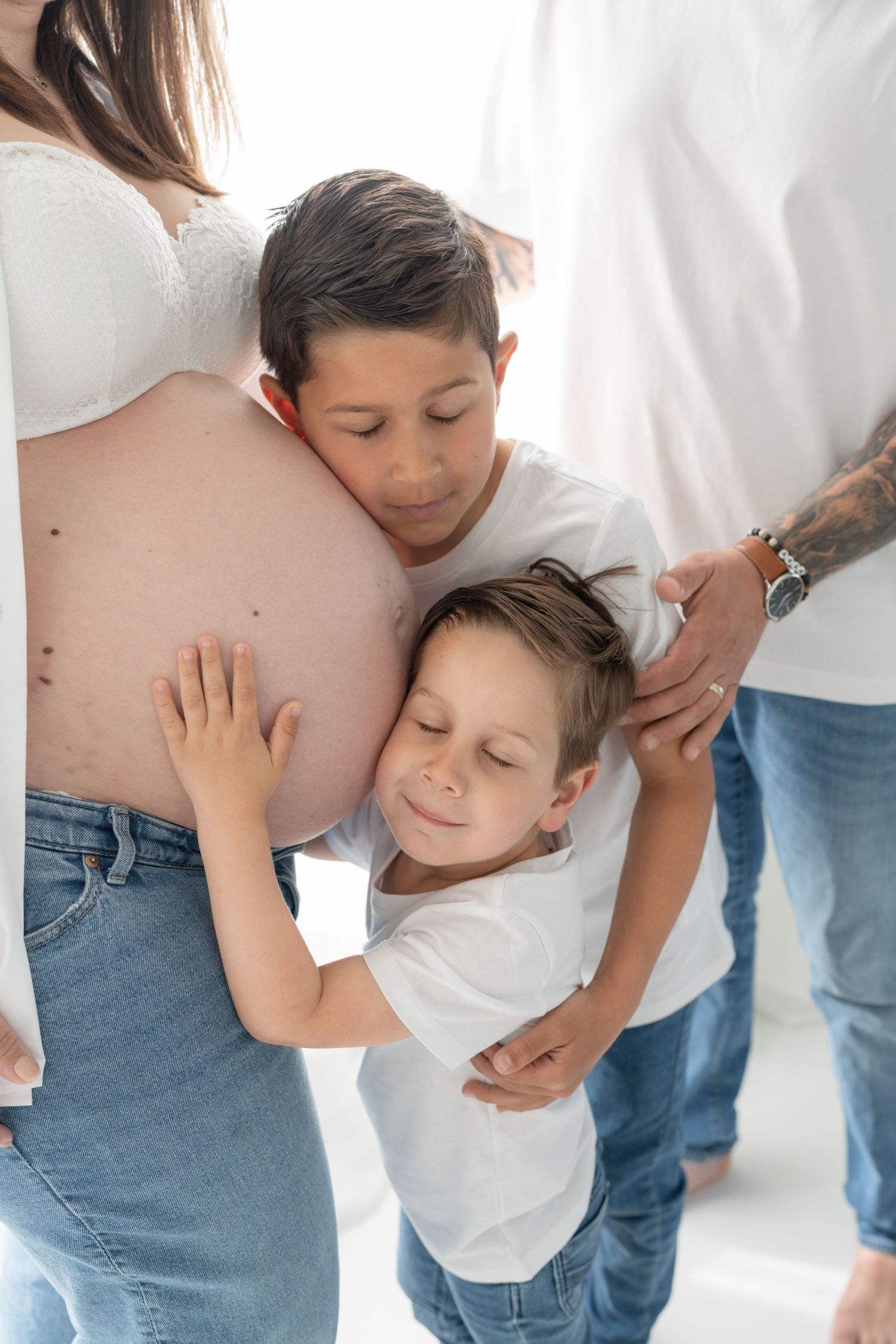 Grands frères donnant un câlin au ventre de leur maman en fermant les yeux et en imaginant leur petit frère qui sera bientôt avec eux