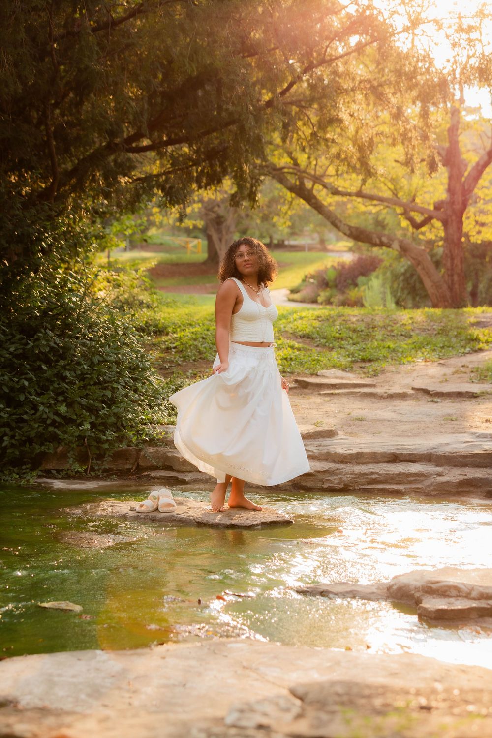 A flowing white dress twirls gracefully during golden hour in a scenic outdoor setting with stone paths and water features.