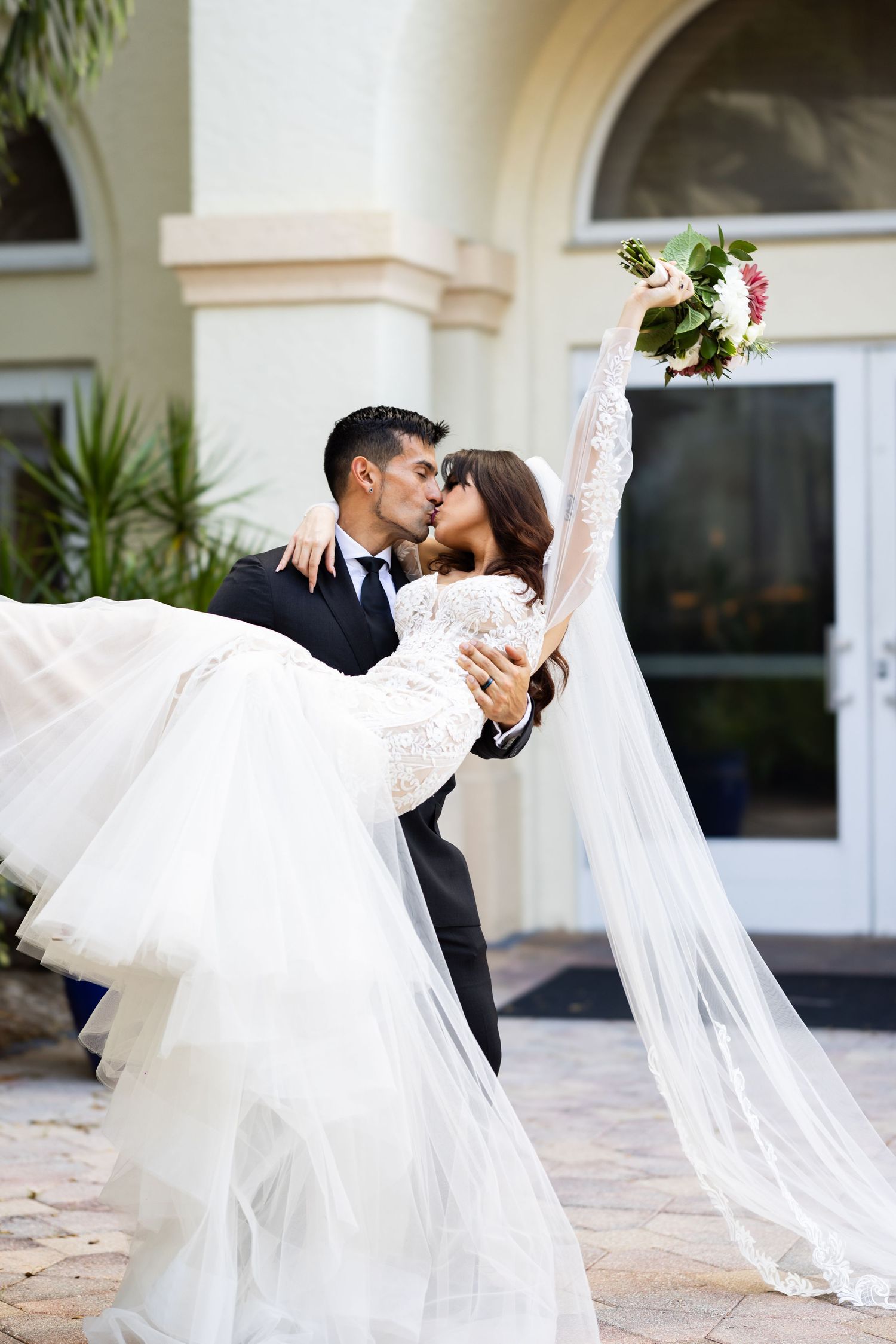 A romantic dip kiss between newlyweds with the bride's flowing white veil and dress creating elegant movement.