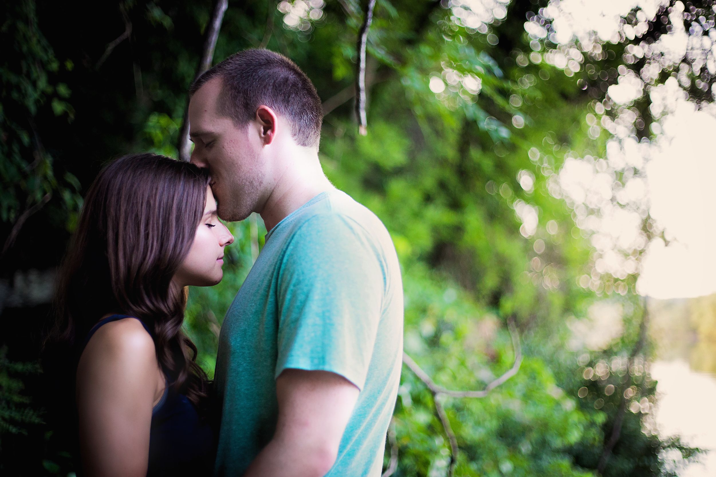 A couple shares a tender moment in front of lush green foliage.