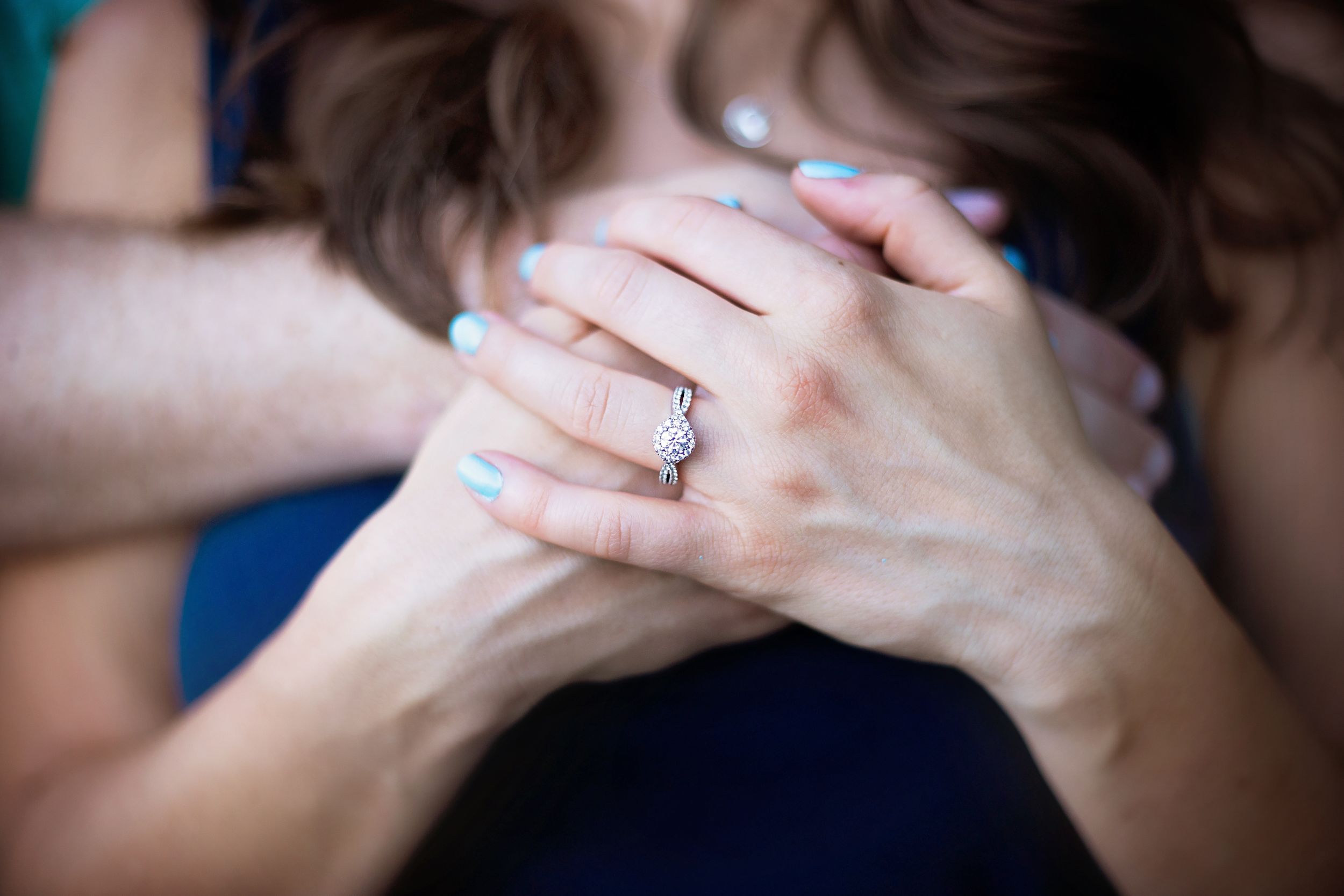 Close-up of hands showcasing an engagement ring with interlocked fingers.