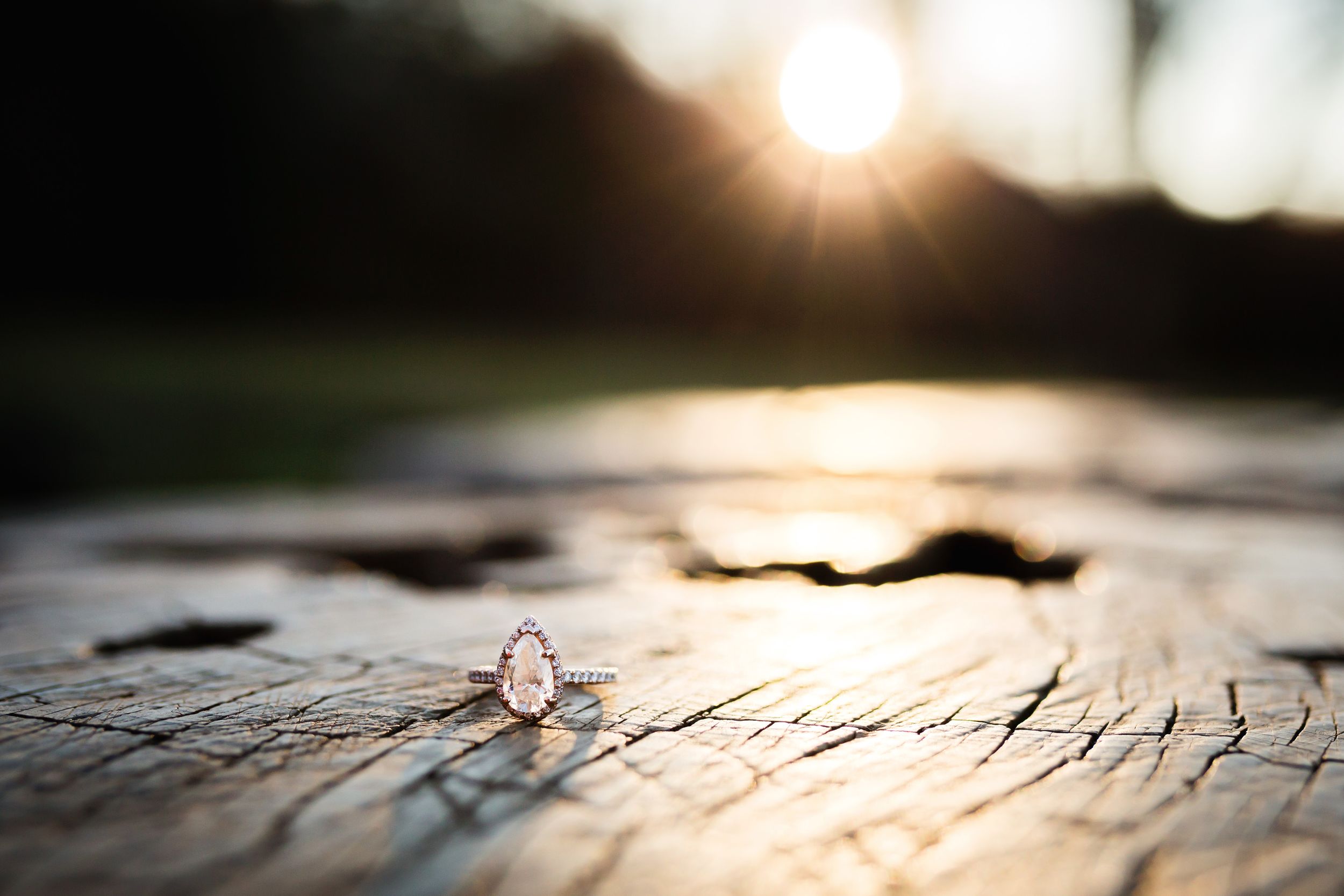 A delicate engagement ring sparkles on weathered wood during sunset.