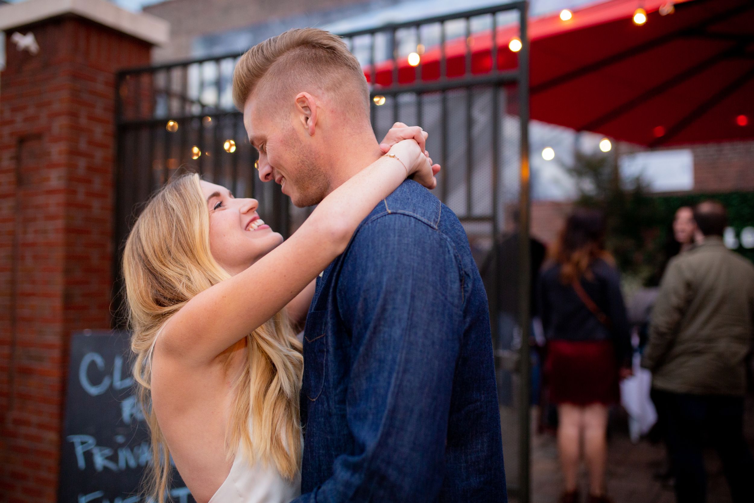 A couple shares an intimate dance moment under outdoor string lights.