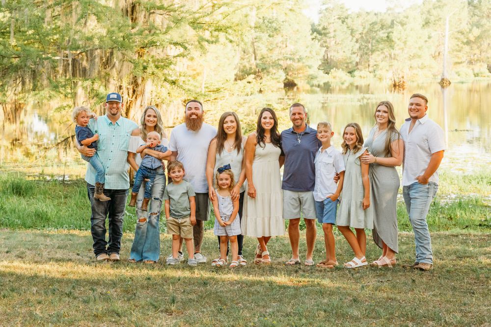 A group in coordinated blue and neutral colored outfits poses together outdoors in a sunlit wooded setting.