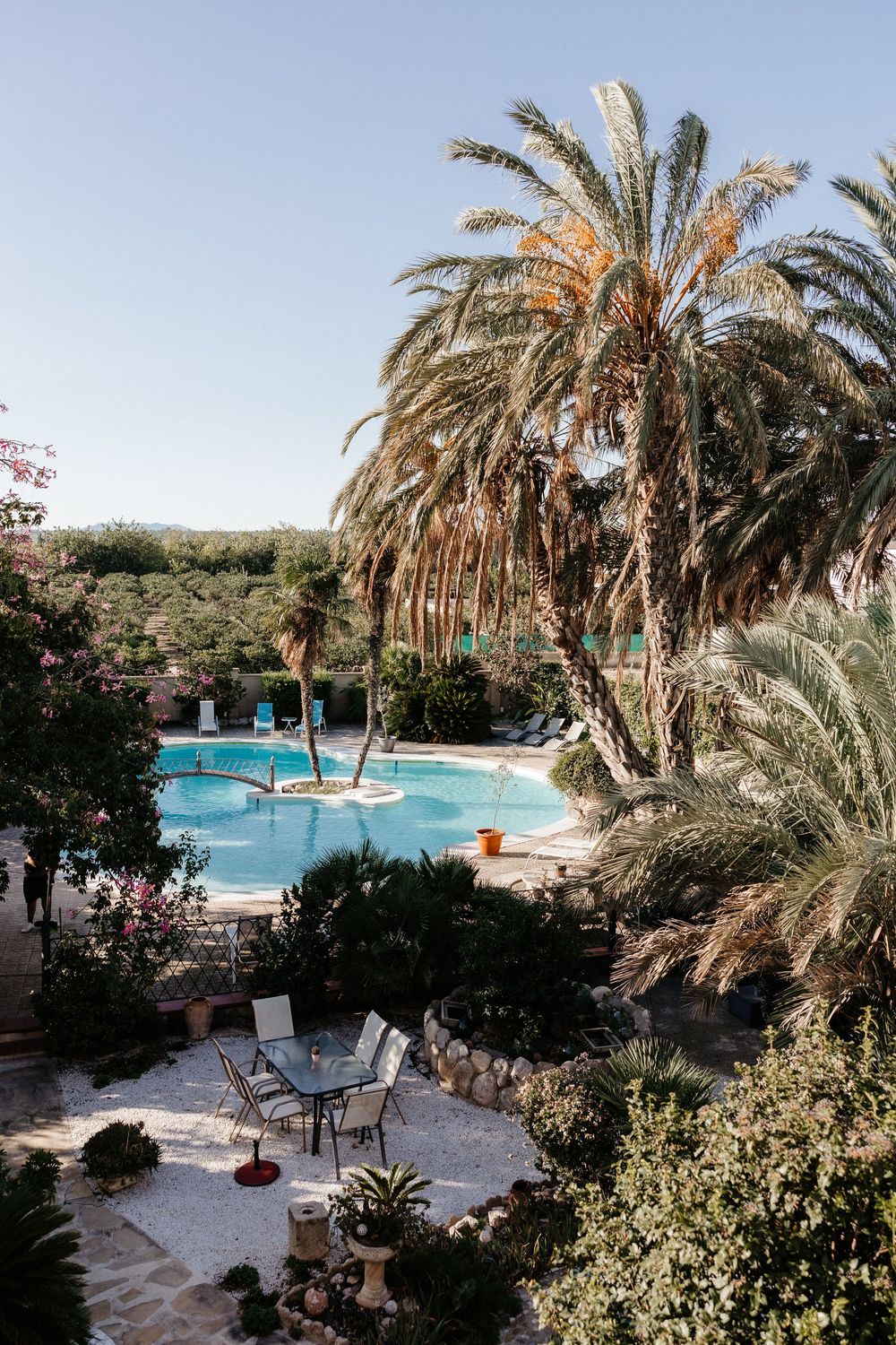 Luxurious resort swimming pool surrounded by palm trees and stone pathways with lounge chairs in a tropical setting.