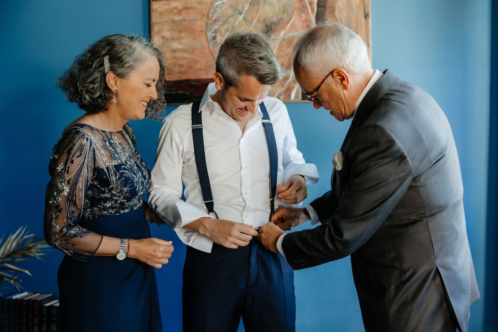 Three people share a joyful moment as they gather together against a bright blue wall.