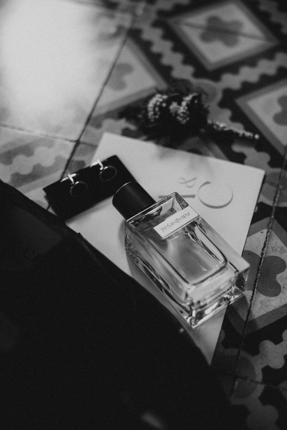 A black and white photograph of perfume bottles arranged diagonally with dramatic shadows and lighting.