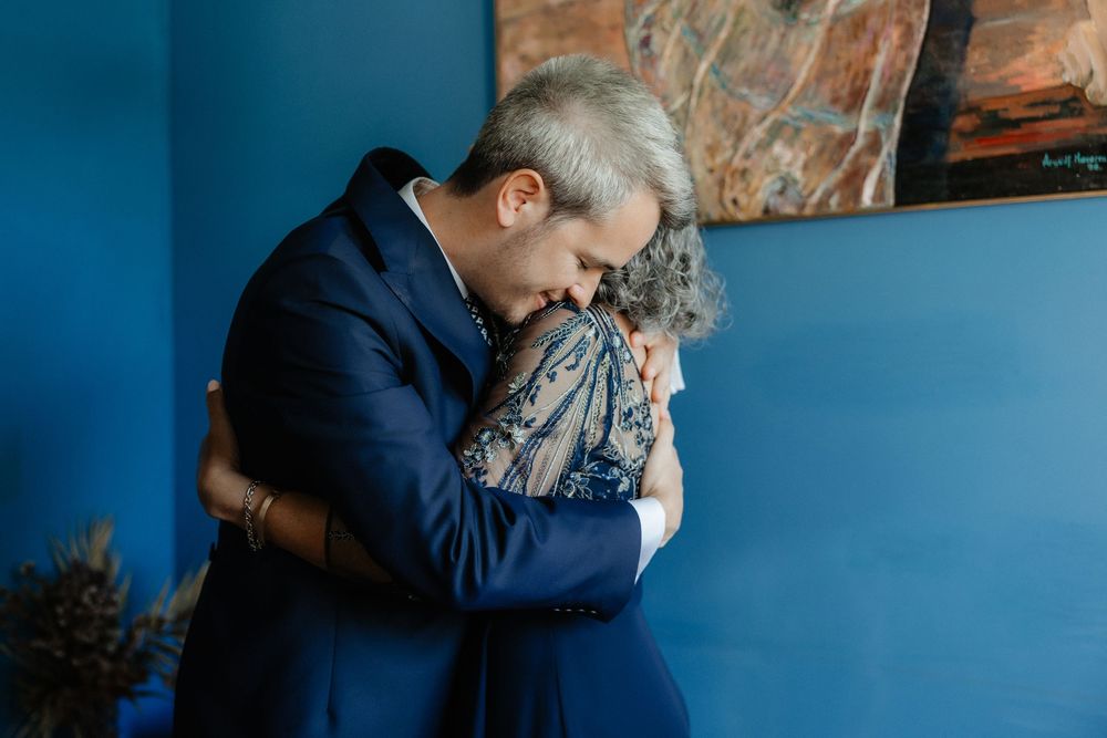 A couple in formal attire shares a romantic embrace against a blue-toned backdrop.