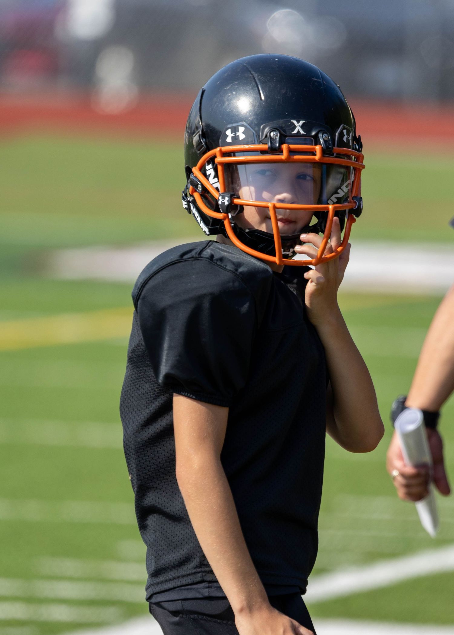 Youth football player in black uniform with Under Armour helmet on field.