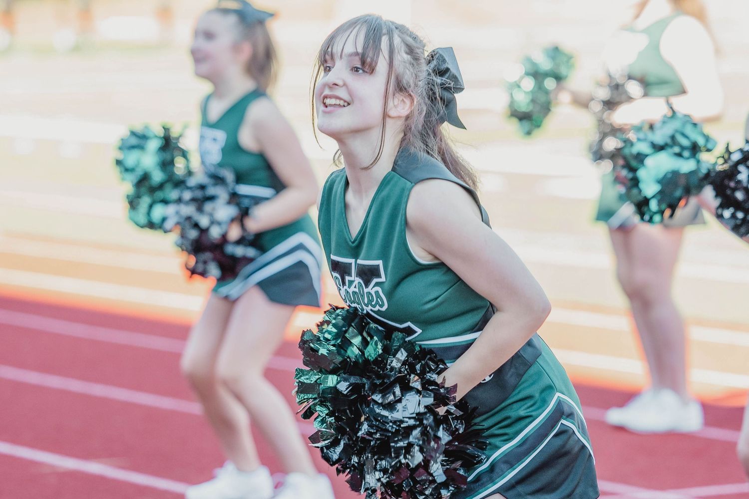Cheerleaders in green uniforms performing with pom poms on a track field.