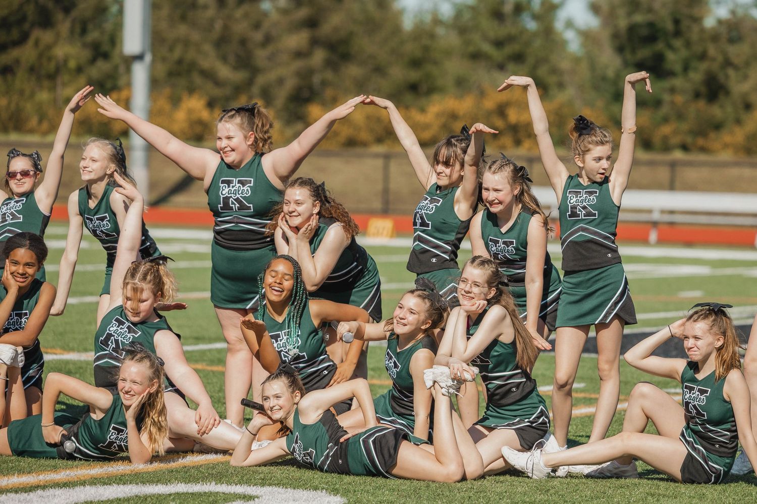 Group of cheerleaders in green uniforms posing together on a sports field.