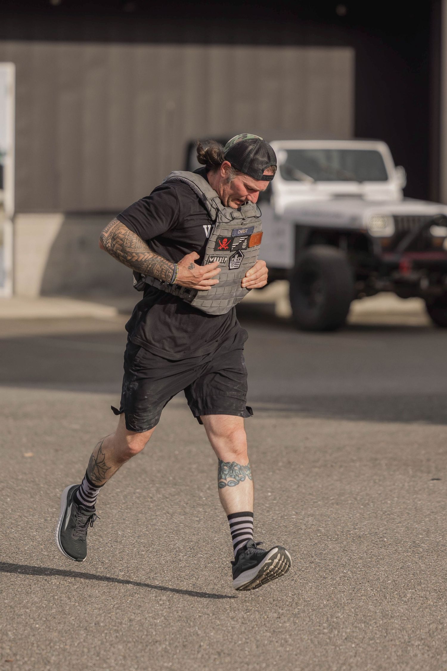 Athlete in dark clothing running outdoors with tattoos visible on arms and legs.