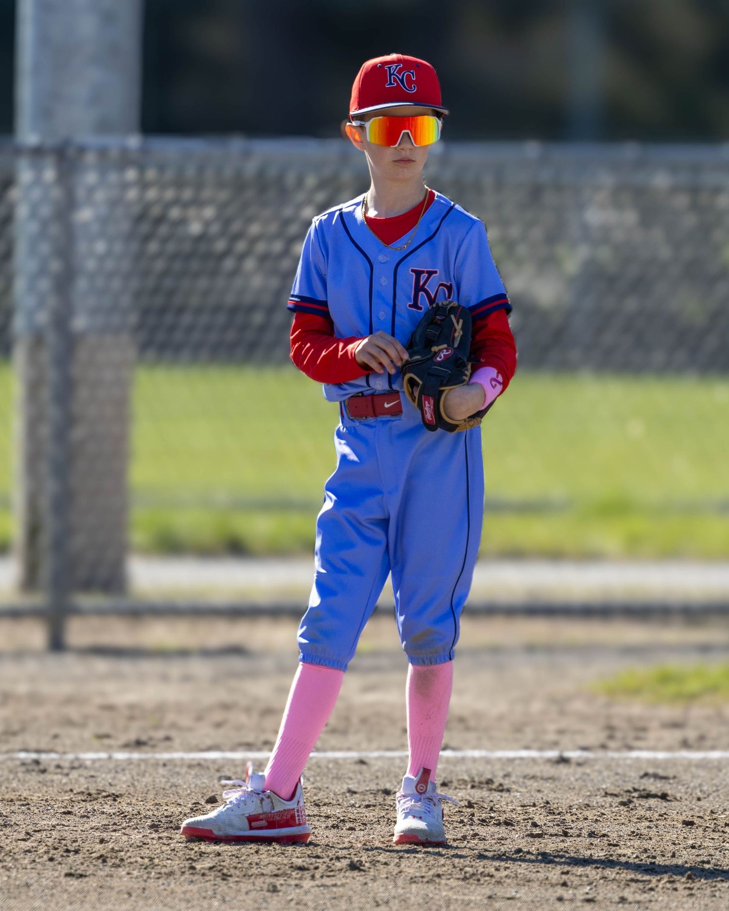 Youth baseball player in blue uniform with pink socks stands ready on the field.
