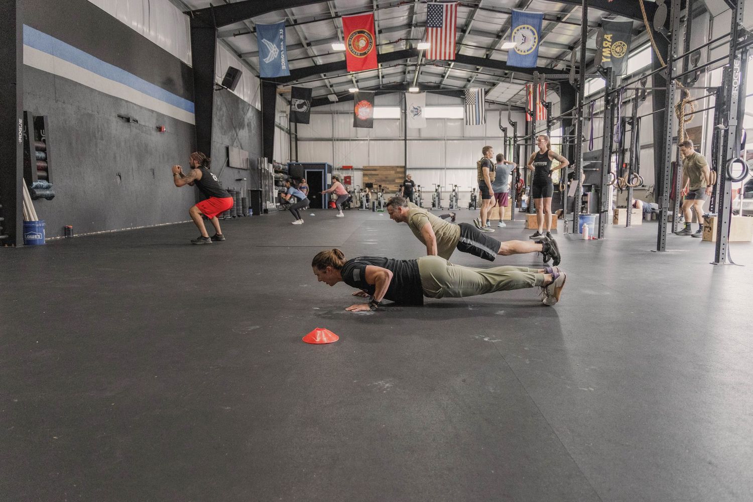 Athletes doing planks and exercises on the floor of a spacious CrossFit gym facility.
