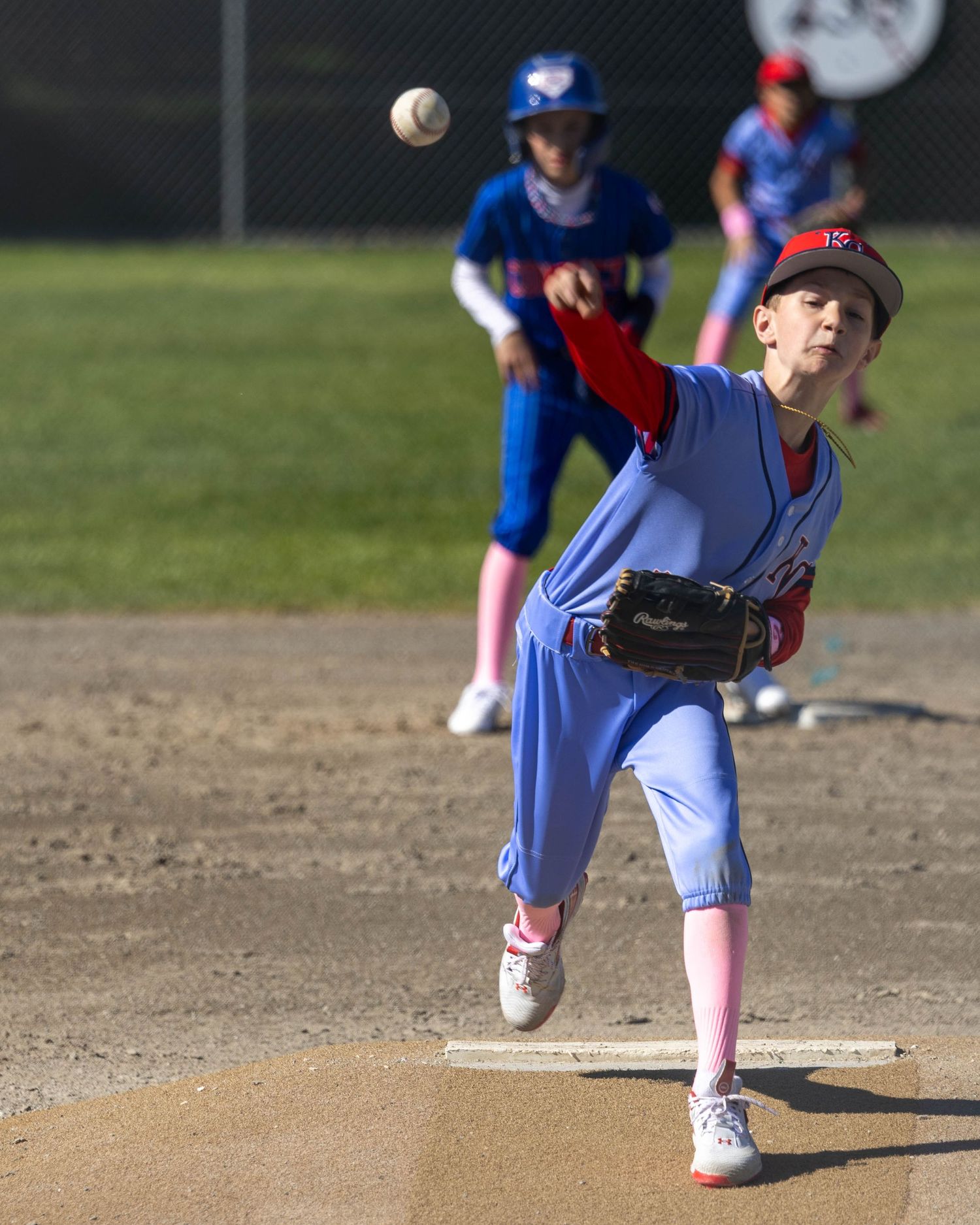 Young baseball pitcher in mid-delivery throwing a pitch from the mound during a game.
