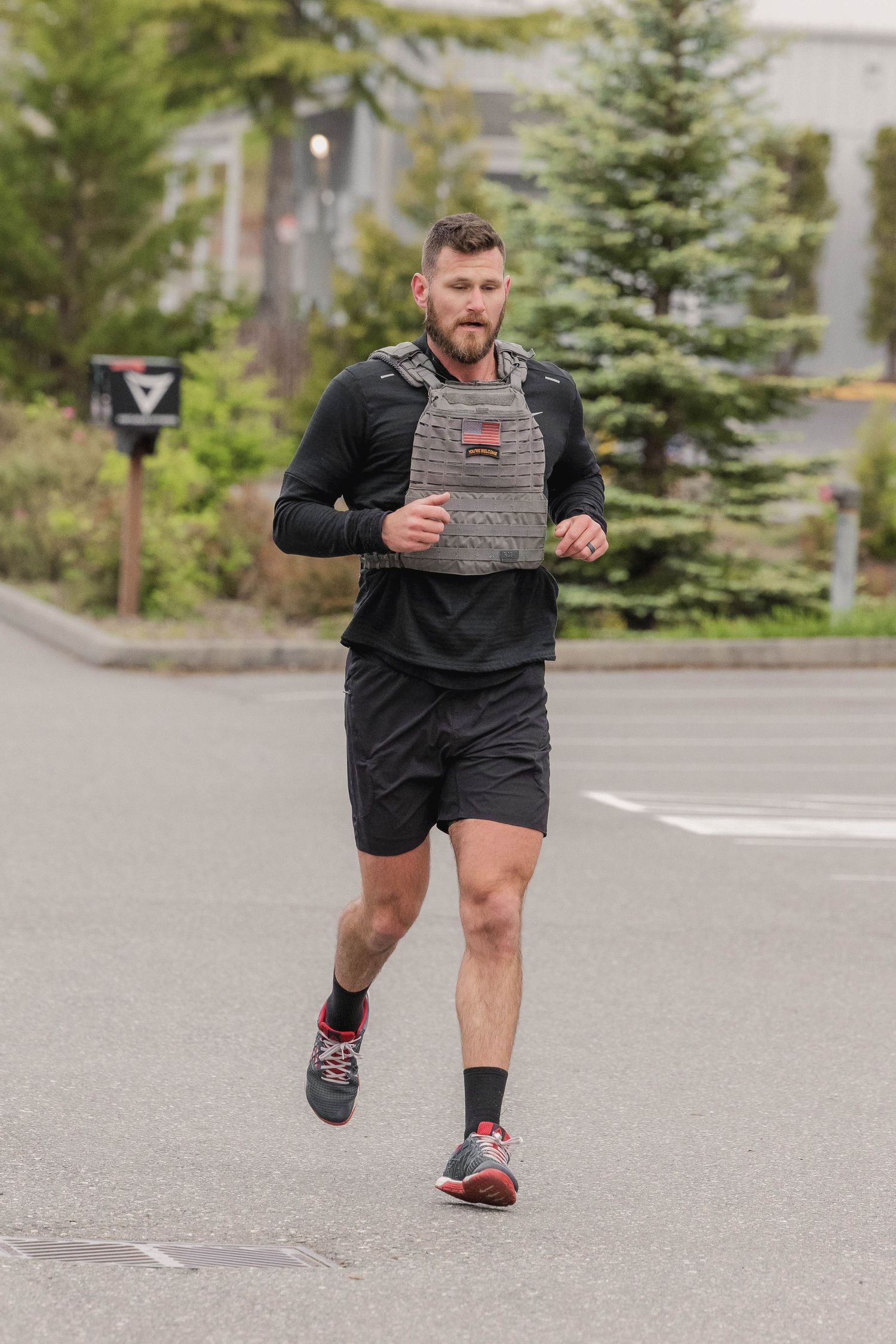 Runner in black athletic wear and gray tactical vest jogging on suburban street.