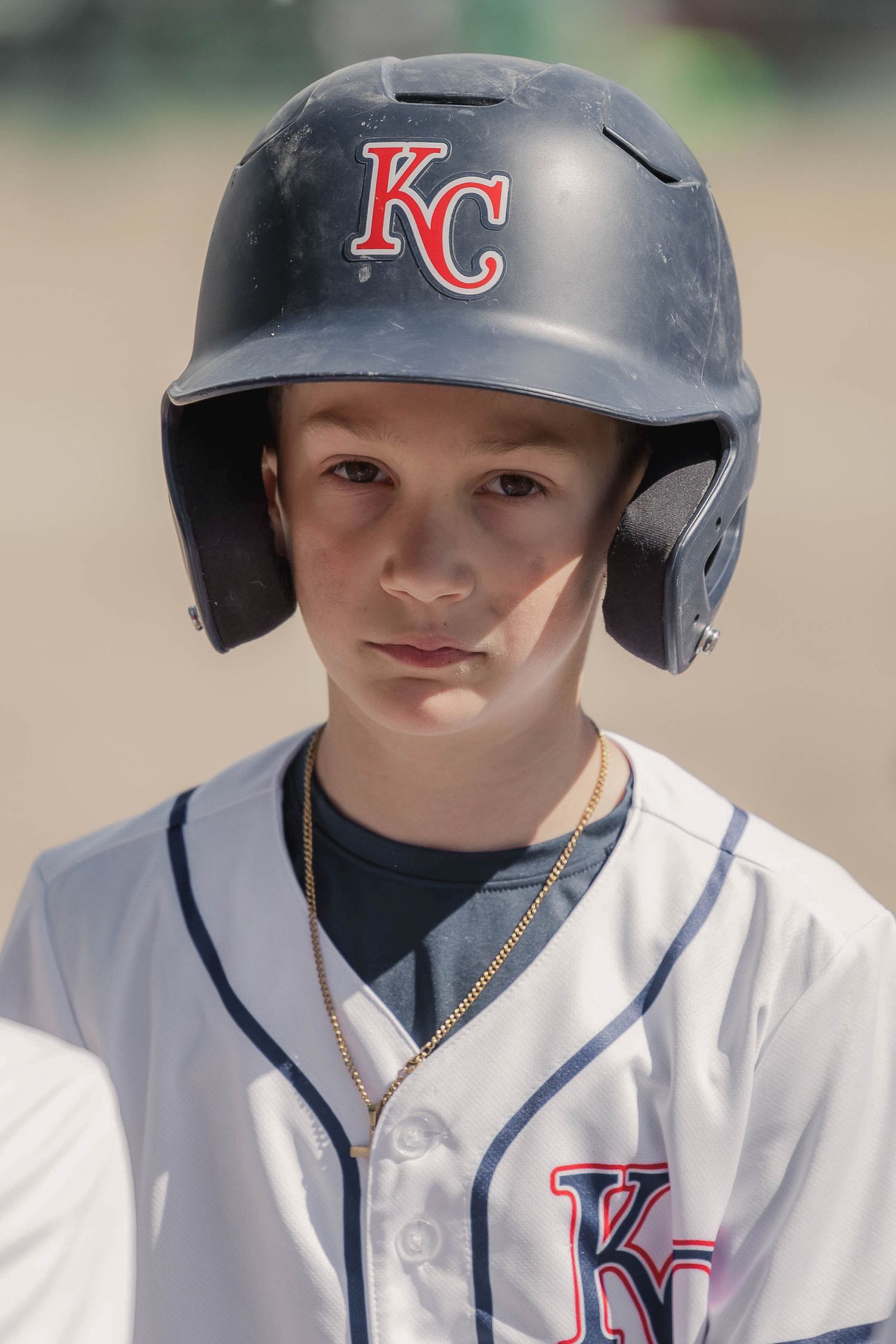 Youth baseball player wearing a KC baseball helmet and white uniform.