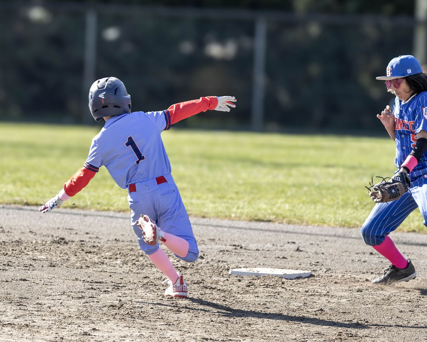 Youth baseball player sliding into base during a game while opponent reaches for the tag.