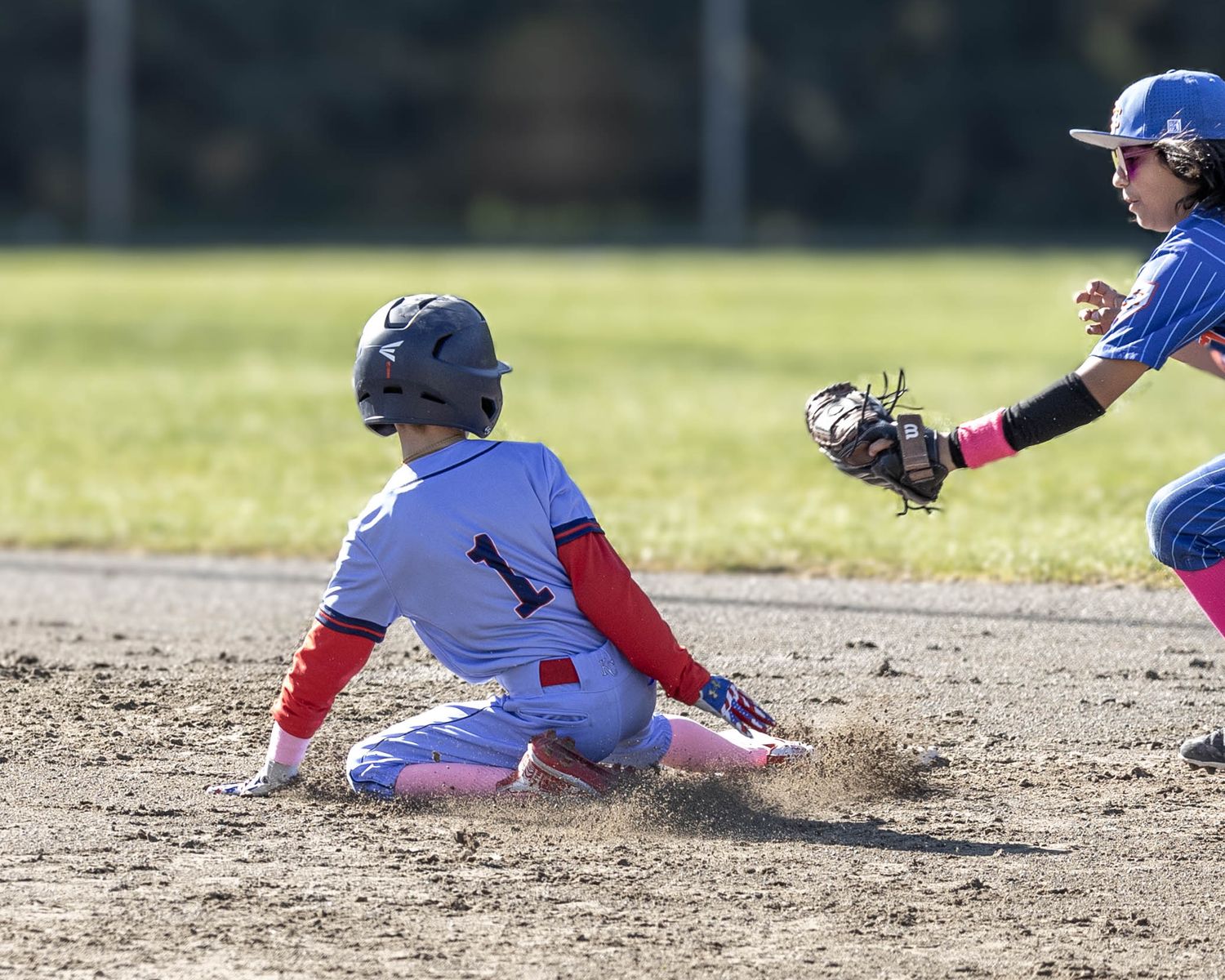 Baseball player in grey uniform slides into base as defender attempts to make the play.