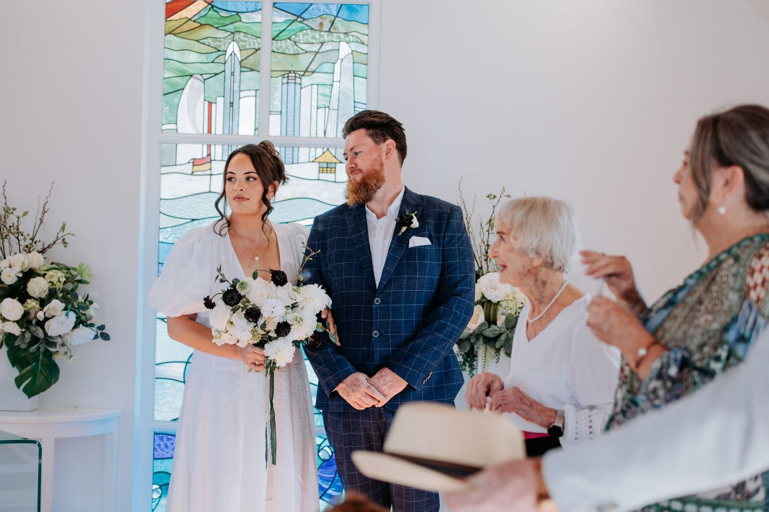 Wedding ceremony in progress inside white chapel with elegant decor.