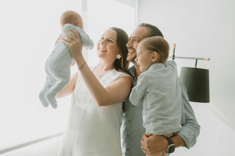 Joyful family moment with everyone dressed in light colors against white wall.