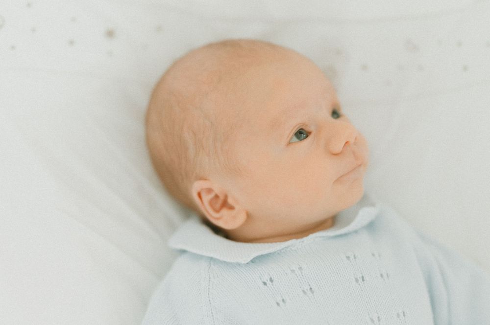Newborn wearing light blue outfit lying on white surface.