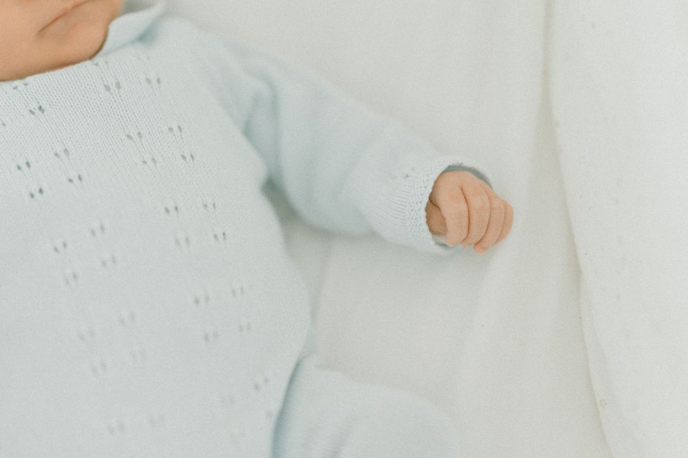 Close-up of tiny hand and light blue onesie with pattern details.