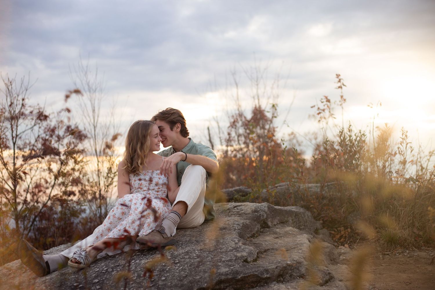 A tender romantic moment between two people sitting on a rocky outcrop during golden hour at sunset at Sassafrass Mountain, South Carolina.