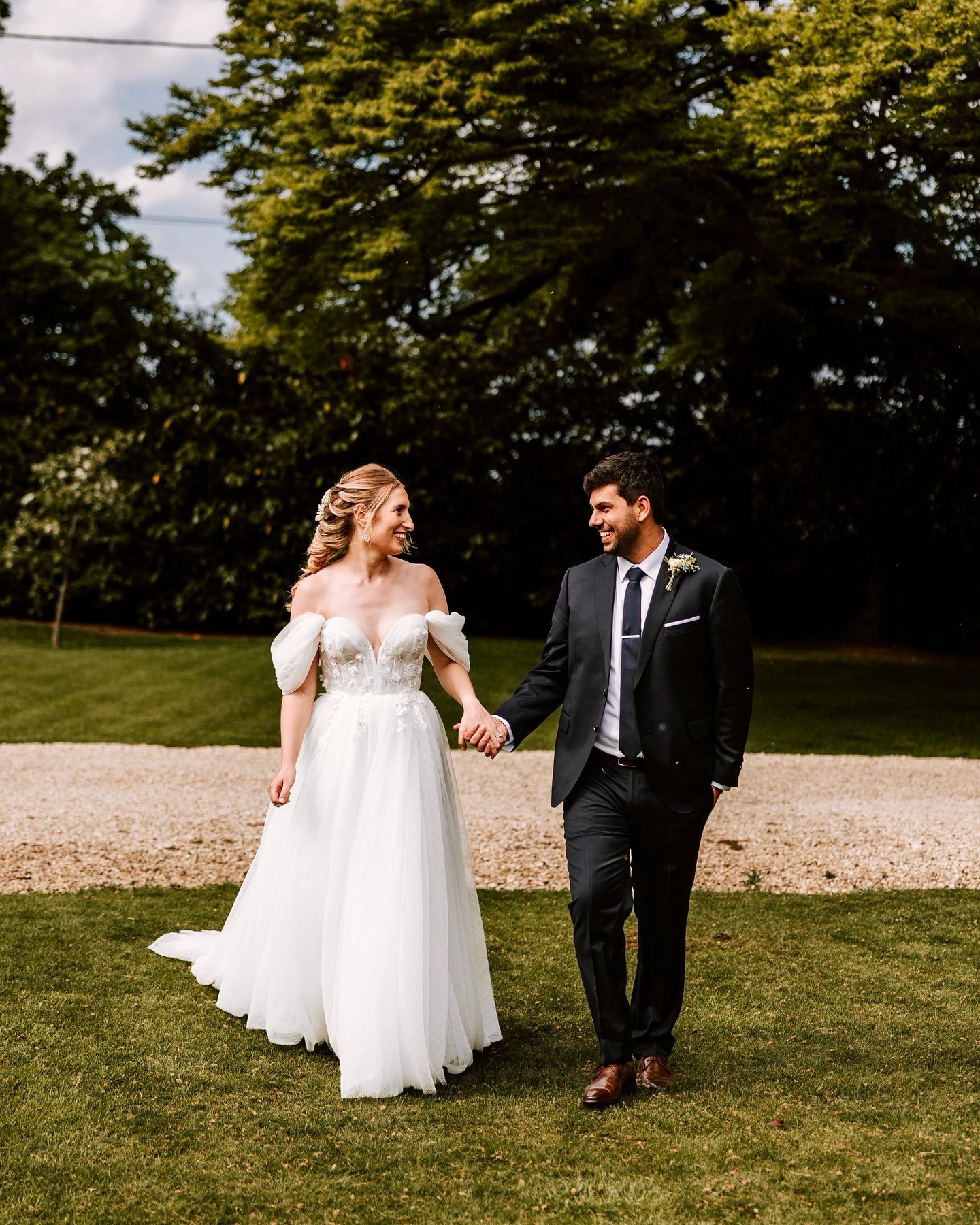 Newlyweds walking together across a grassy outdoor venue in elegant wedding attire.