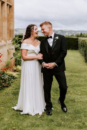 Candid wedding moment of a couple laughing together on a grassy hillside.