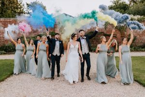 A wedding party celebration with colorful smoke bombs and bridesmaids in sage green dresses.