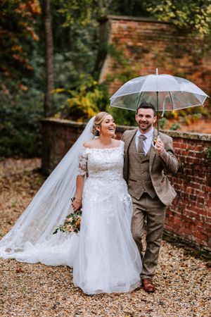 Joyful wedding couple sharing a laugh while holding a clear umbrella on an autumn day.