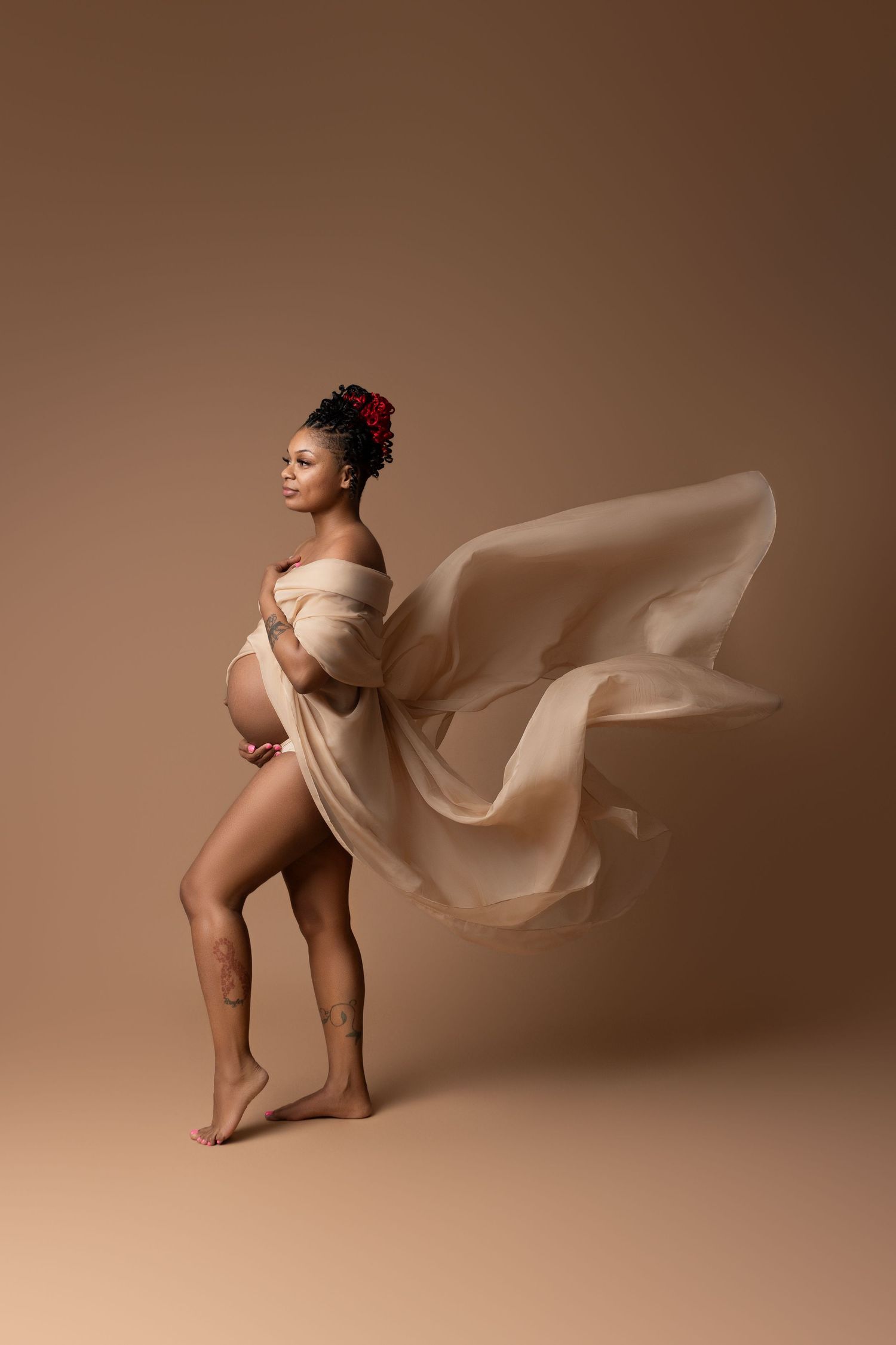 An expectant mom in Cedar Park, TX, poses with tossing fabric flowing behind her