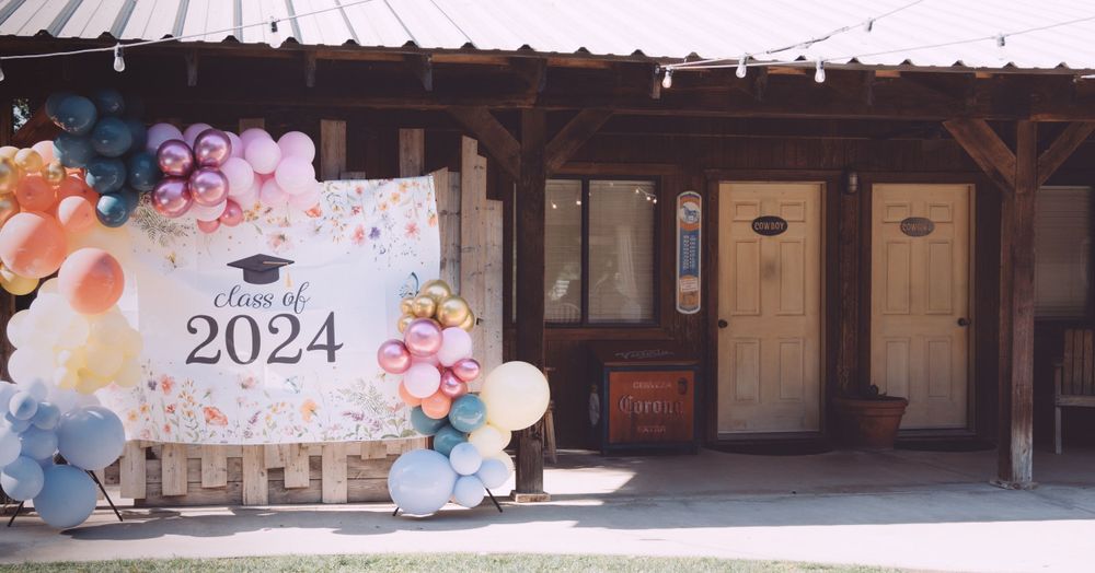 Class of 2024 graduation party backdrop with colorful balloon arch outside rustic barn.