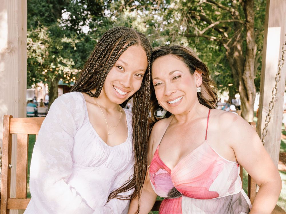 Two women smiling together at an outdoor event in summer dresses.