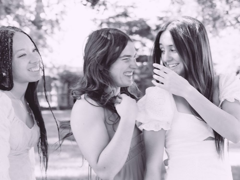 Black and white photo of three young women laughing and smiling together outdoors.