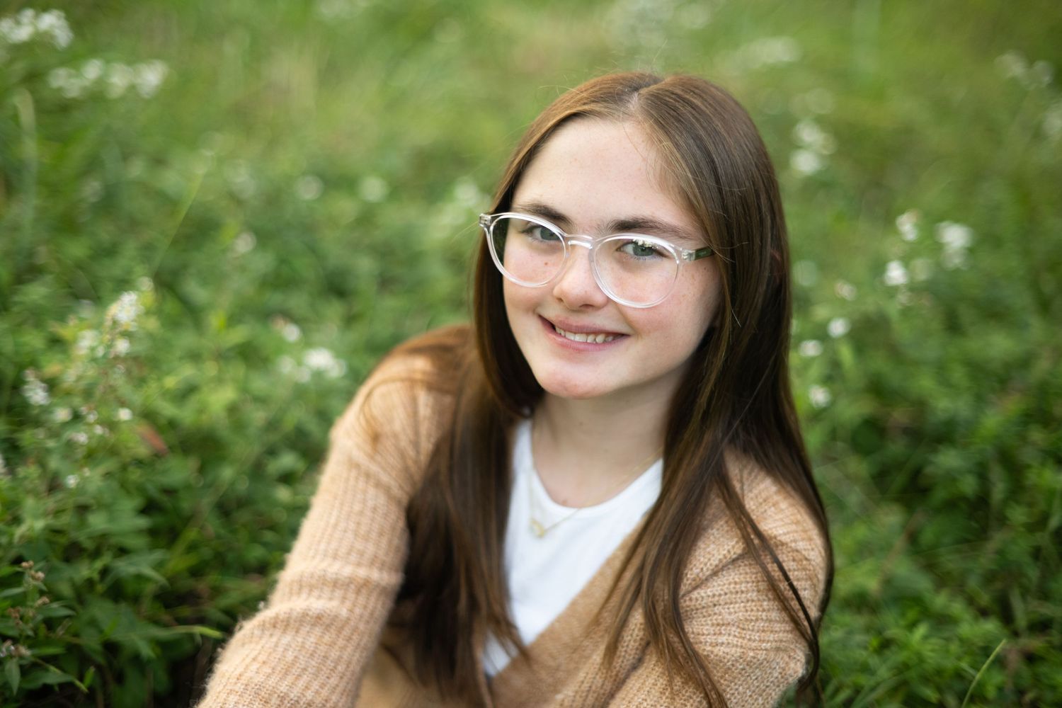 Portrait of person in tan sweater sitting in field of wildflowers.