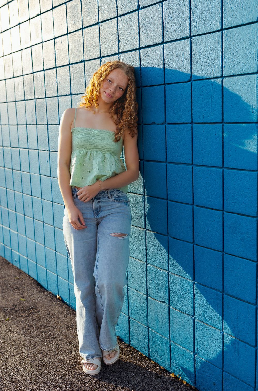 senior girl leaning on blue checkered wall green crop top and jeans curly red hair