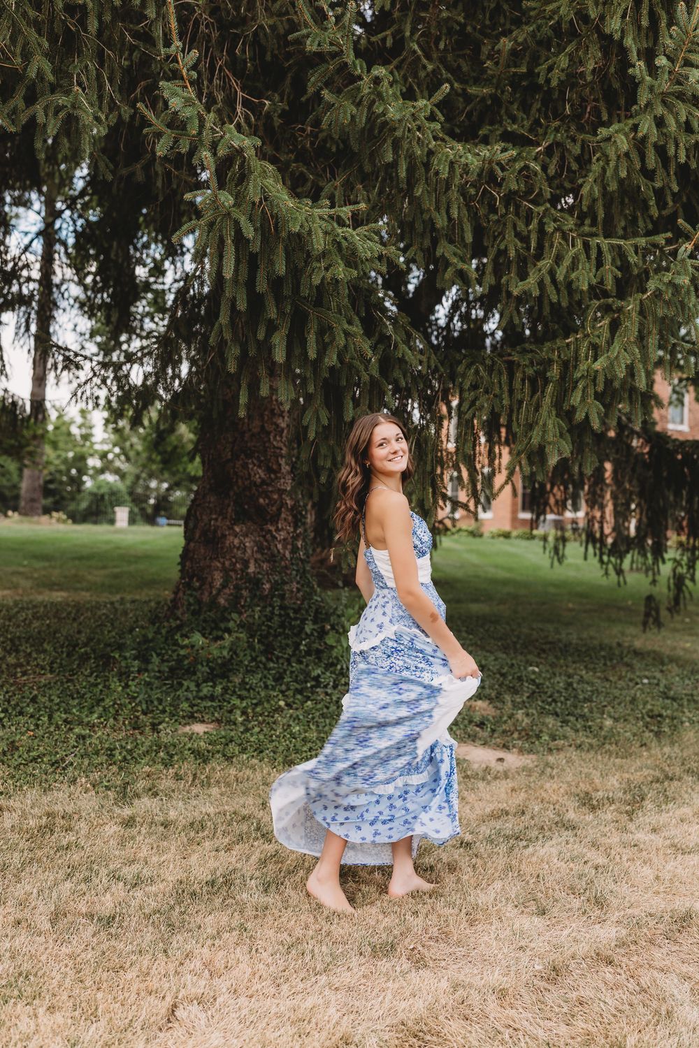 senior girl summer running in blue and white flowy dress looking back over shoulder
