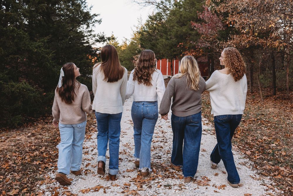 senior girl group in the fall walking down gravel road holding hands laughing