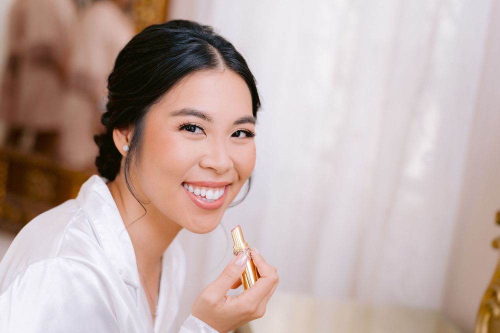 Woman in white robe smiling while applying lip gloss during a beauty routine.
