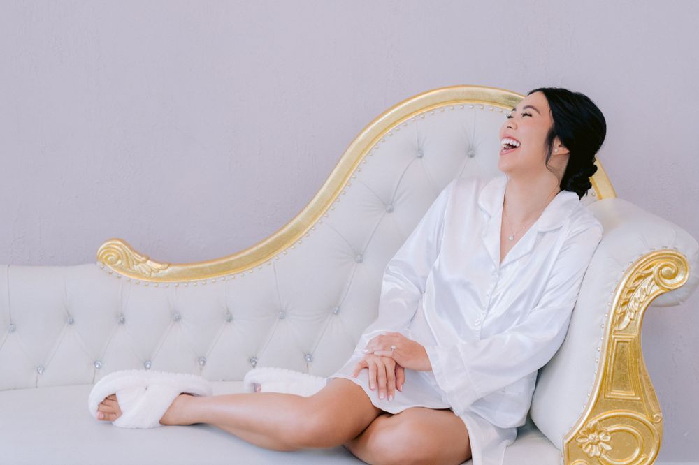 Woman in white robe relaxing on ornate gold and white chaise lounge against light background.