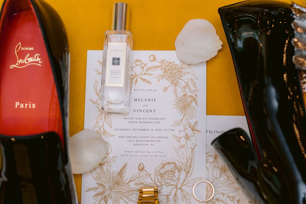 Wedding accessories including shoes, perfume, invitation, and jewelry arranged on a yellow background.