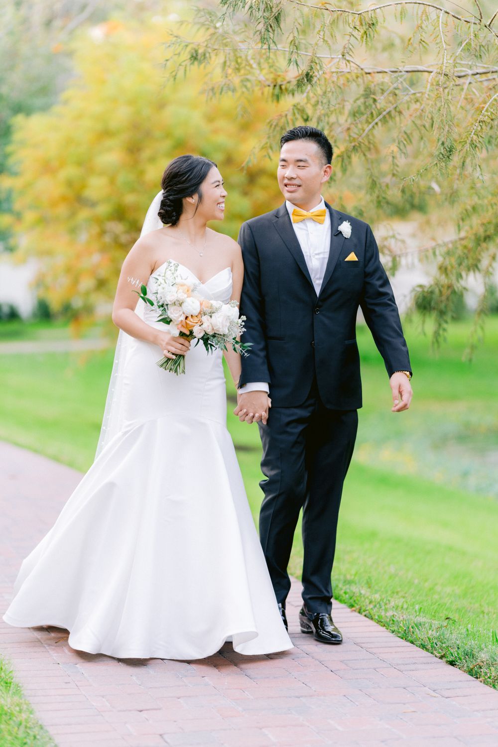 Happy couple walking along a stone path surrounded by lush gardens on their wedding day.