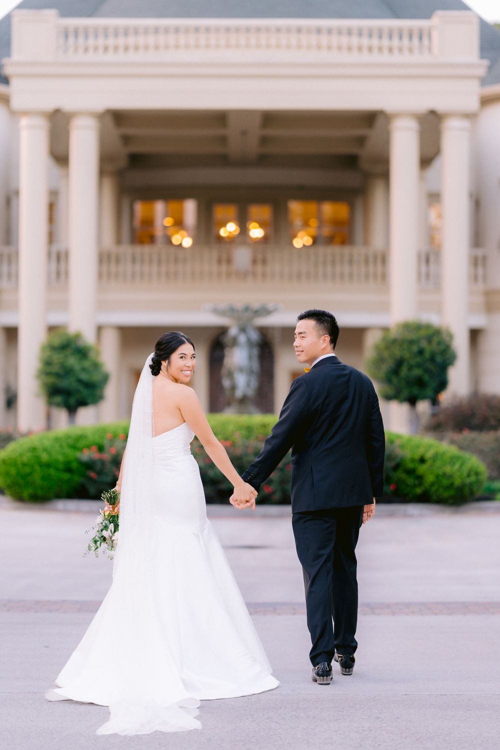 A couple walks hand-in-hand outside a grand columned building during their wedding photoshoot.