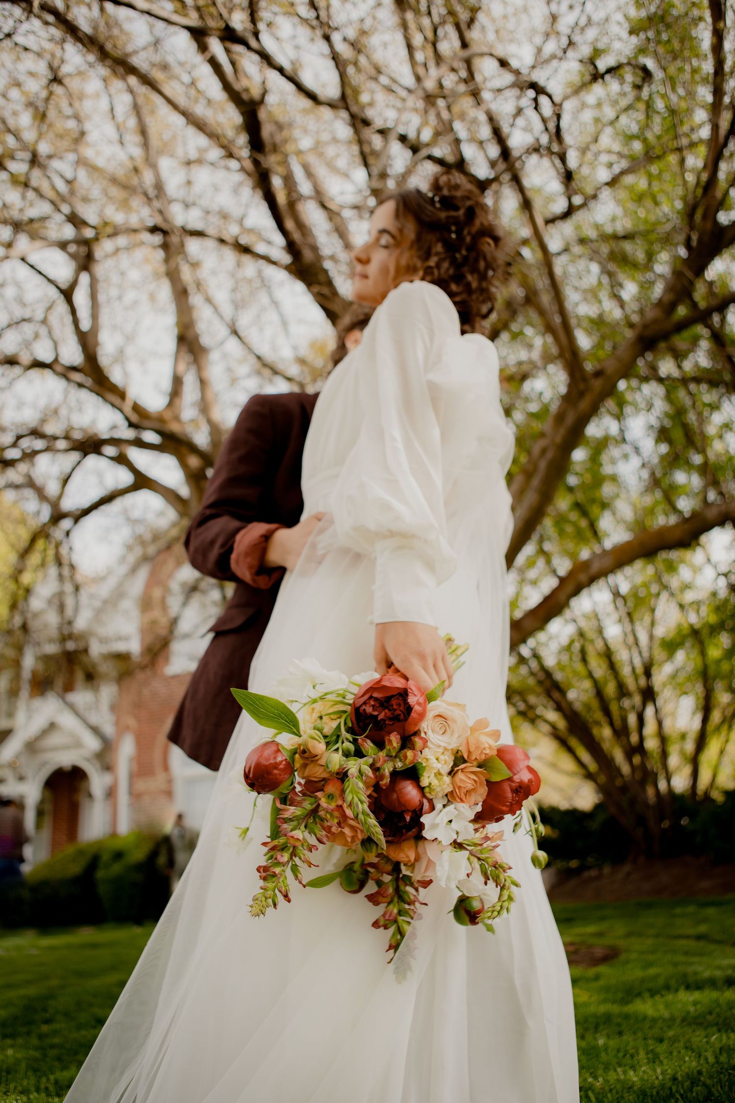 A bride in white holding a vibrant autumn bouquet against a backdrop of trees.