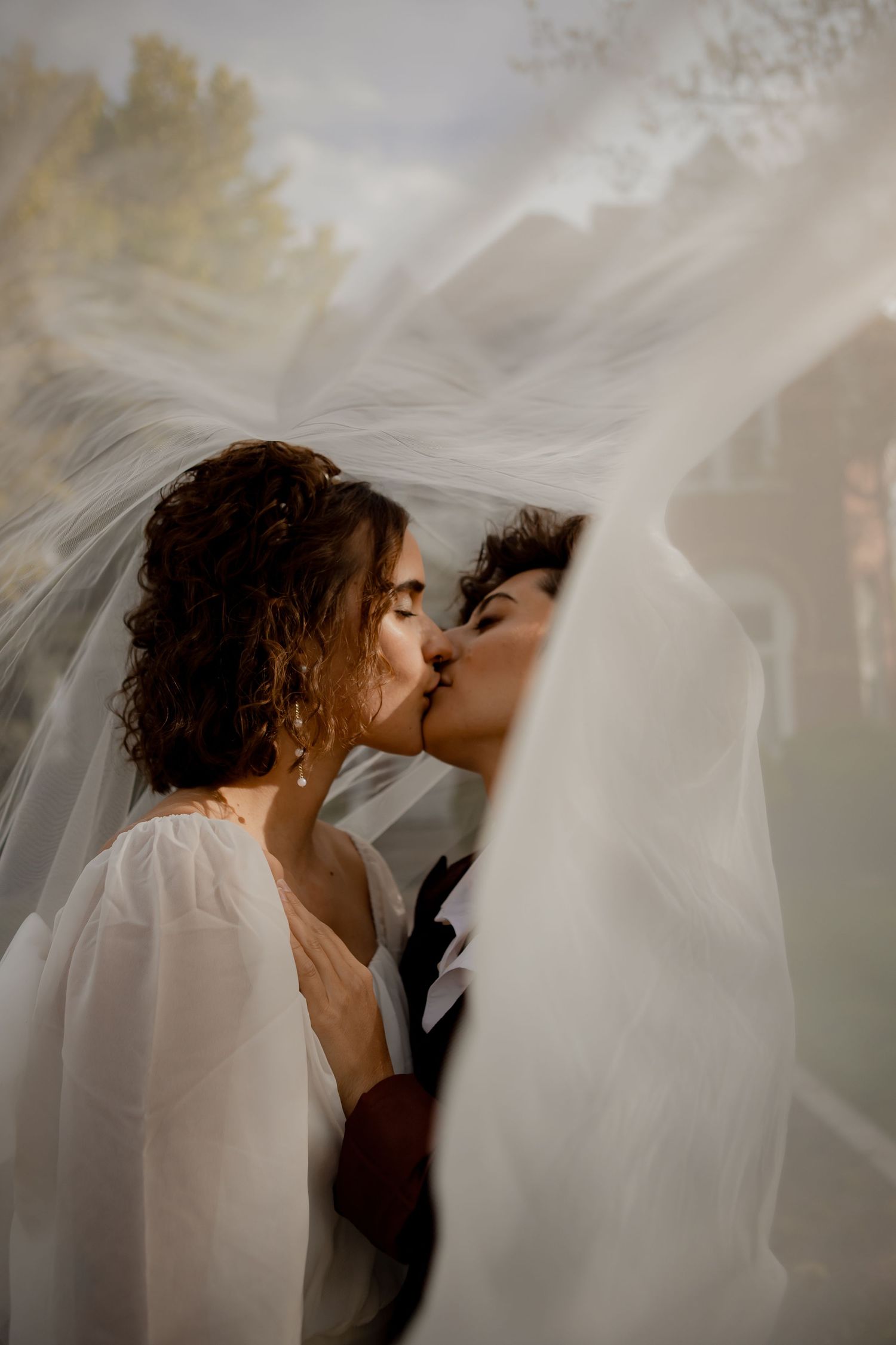 An intimate wedding kiss captured under flowing white veils with ethereal lighting.